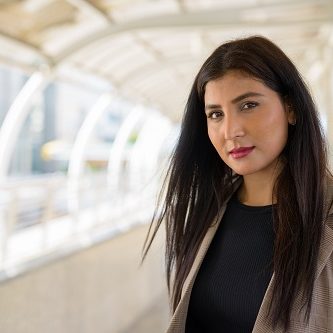 Portrait of young beautiful Indian businesswoman at footbridge in the city outdoors